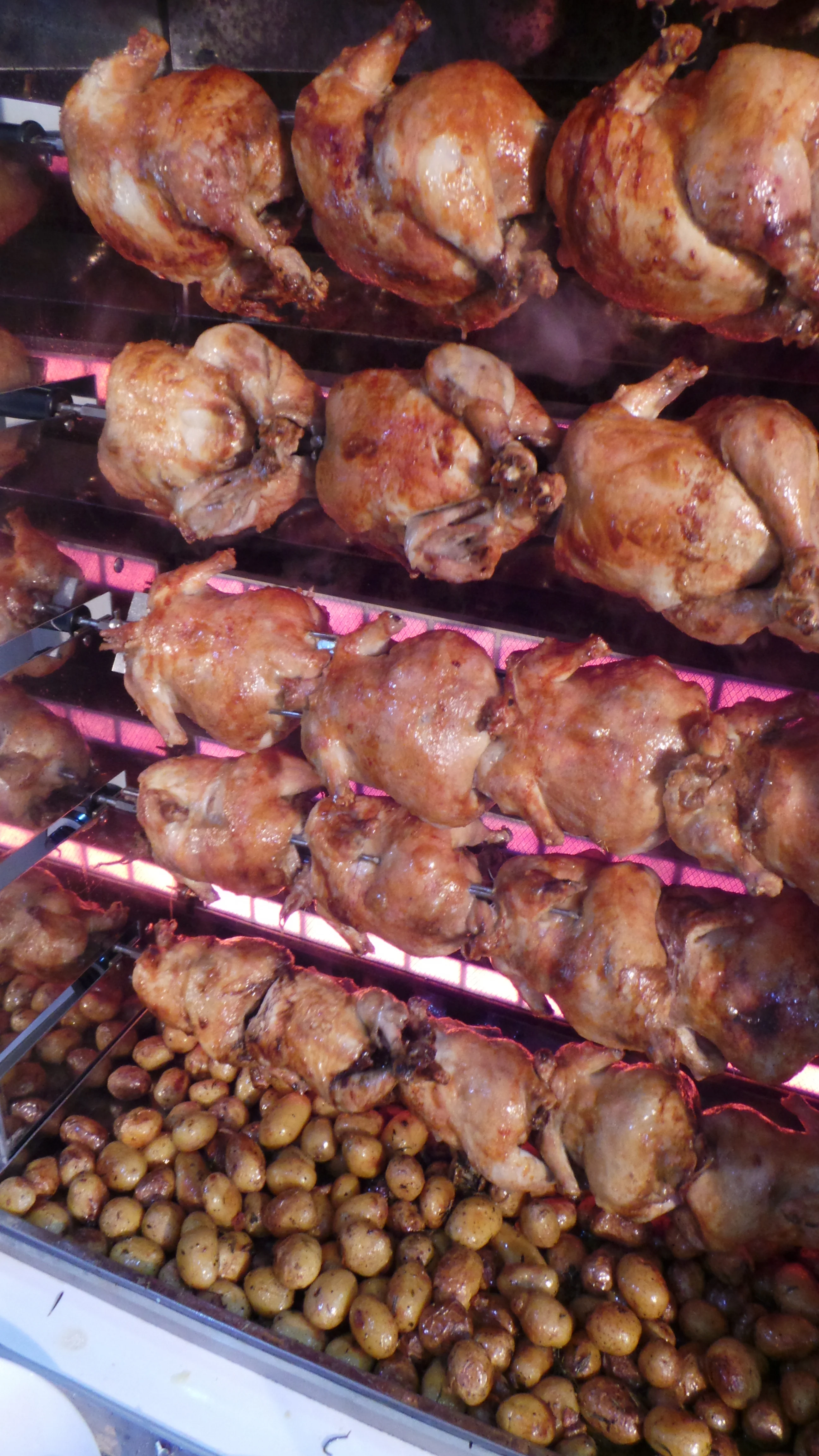 Rows of golden rotisserie chickens spinning on the spit at Tastybirds